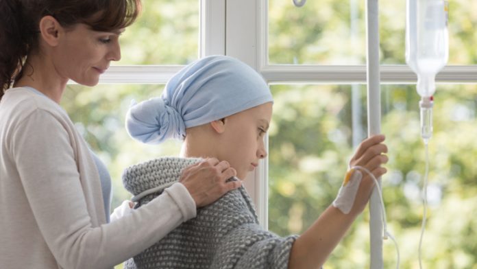 Caregiver hugging sick kid with headscarf holding drip in the hospital
