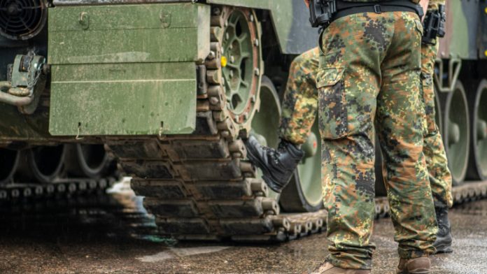Two soldiers in camouflage uniform standing during a break under the rain near the tracks of an armoured tank